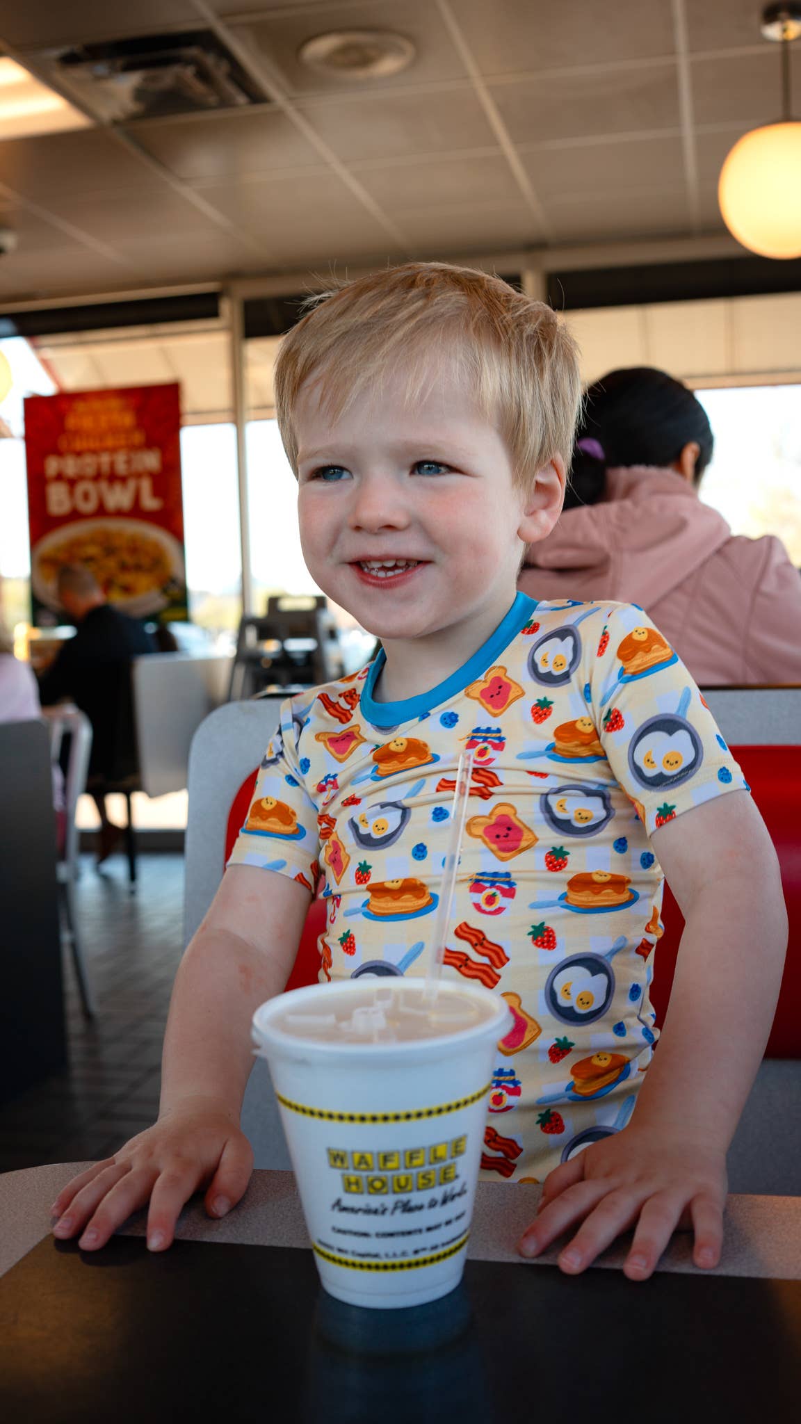 Child in a colorful shirt with a Waffle House cup at a dining table.