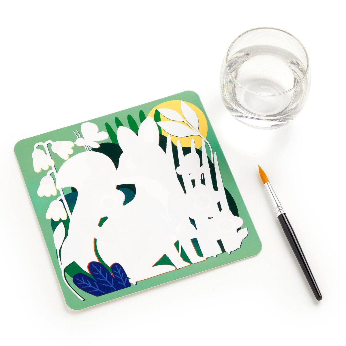 Artistic card with white animal silhouette on a green background, next to a glass of water and paintbrush.