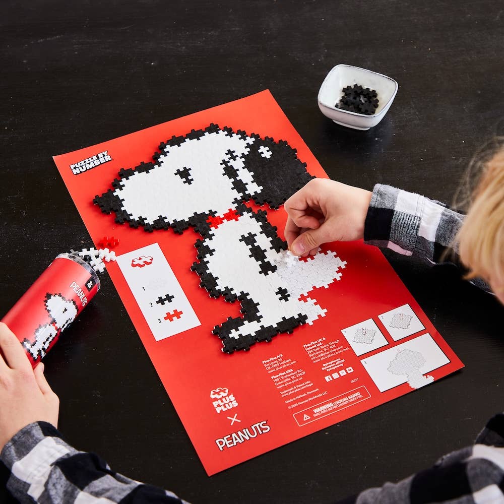 Person assembling a puzzle of a dog, Snoopy,  on a red sheet with 'Peanuts' branding.