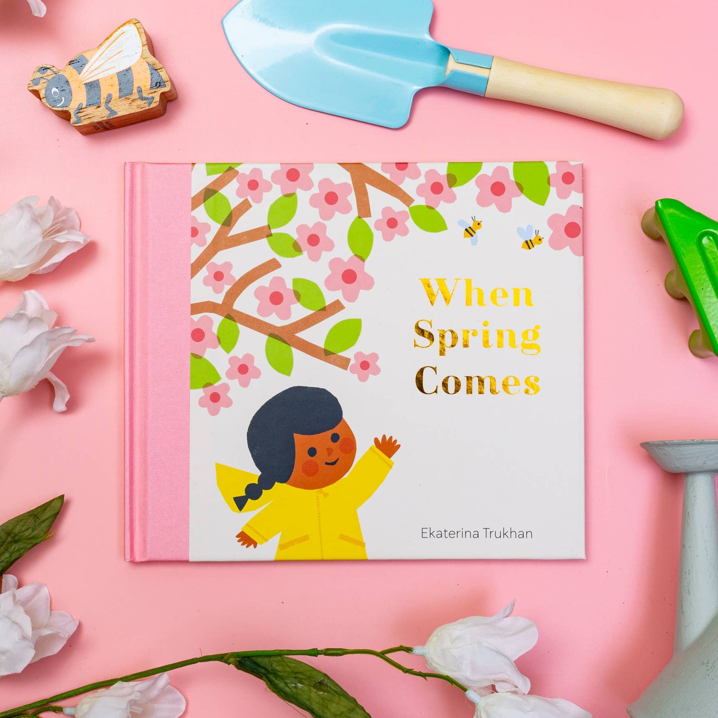 Children's book titled 'When Spring Comes' on a pink background with gardening tools and flowers.