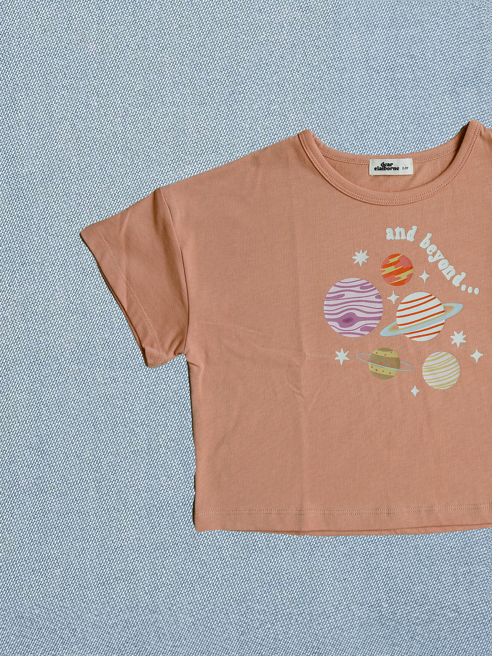 Brown t-shirt with space-themed graphic on a textured blue background