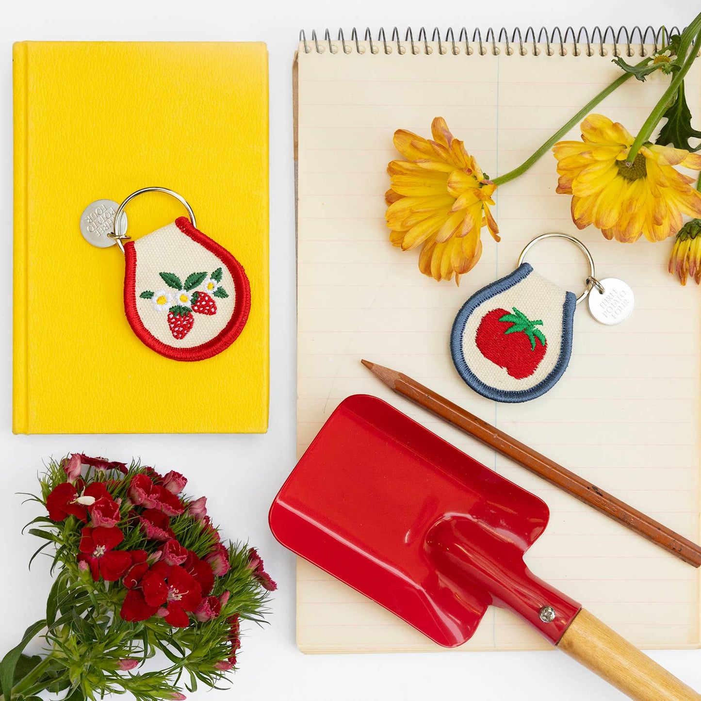 Keychains with strawberry design, red shovel, yellow notebook, and flowers on a white background