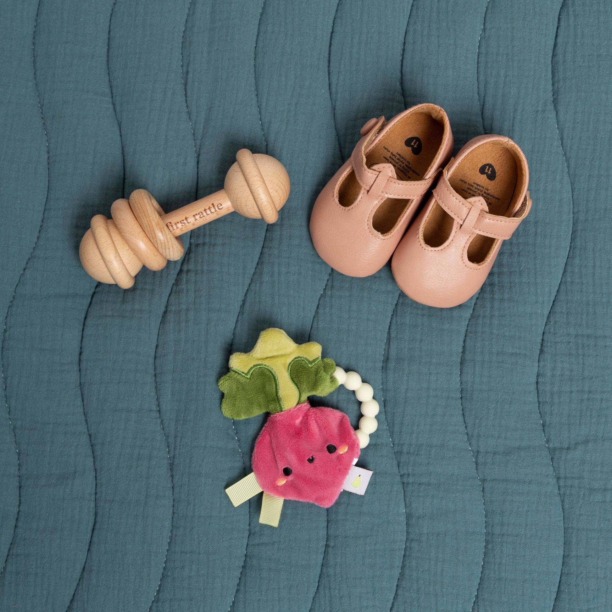 Wooden rattle, pink shoes, and colorful teething ring on a textured teal surface