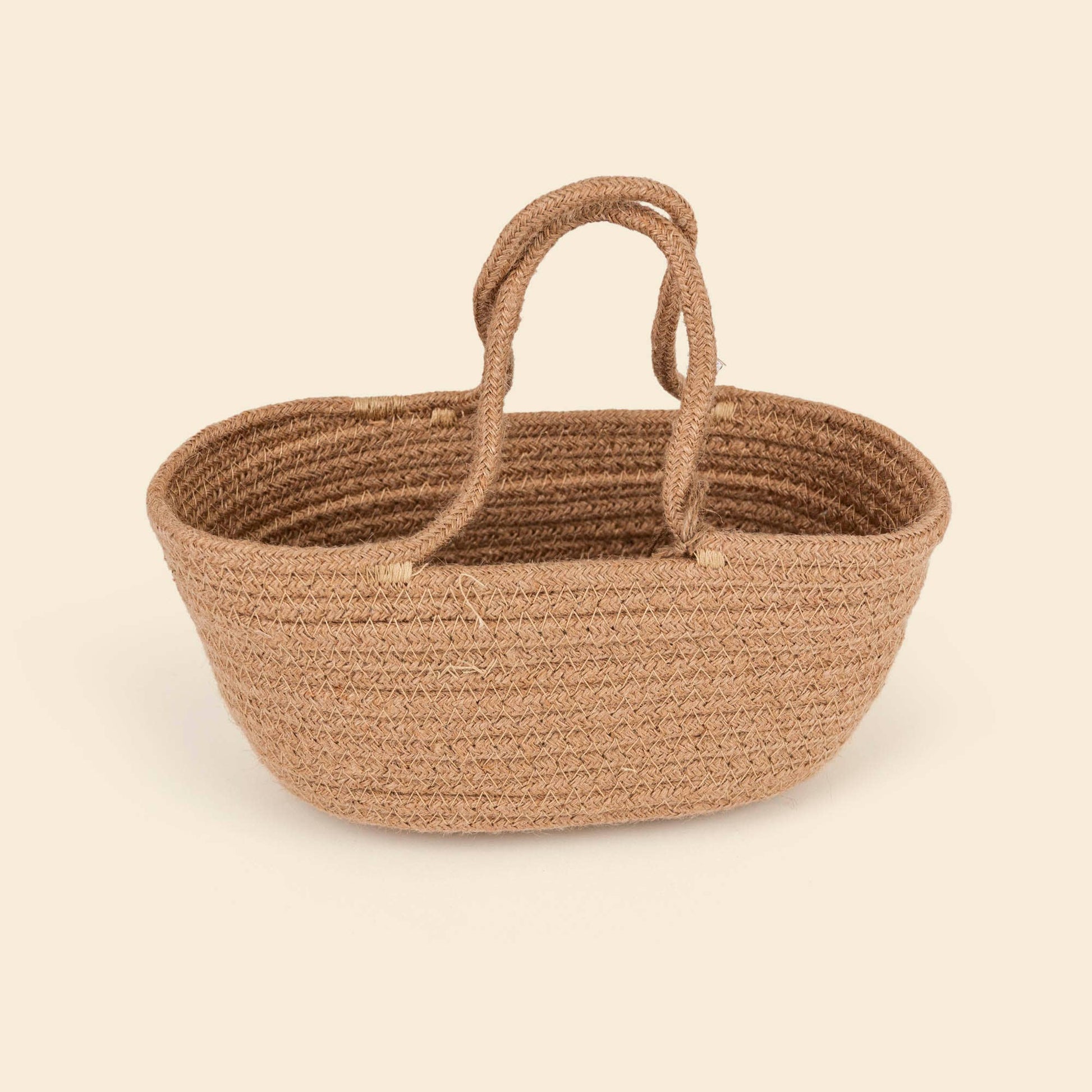 A natural woven jute basket with two loop handles, shown on a solid light beige background.