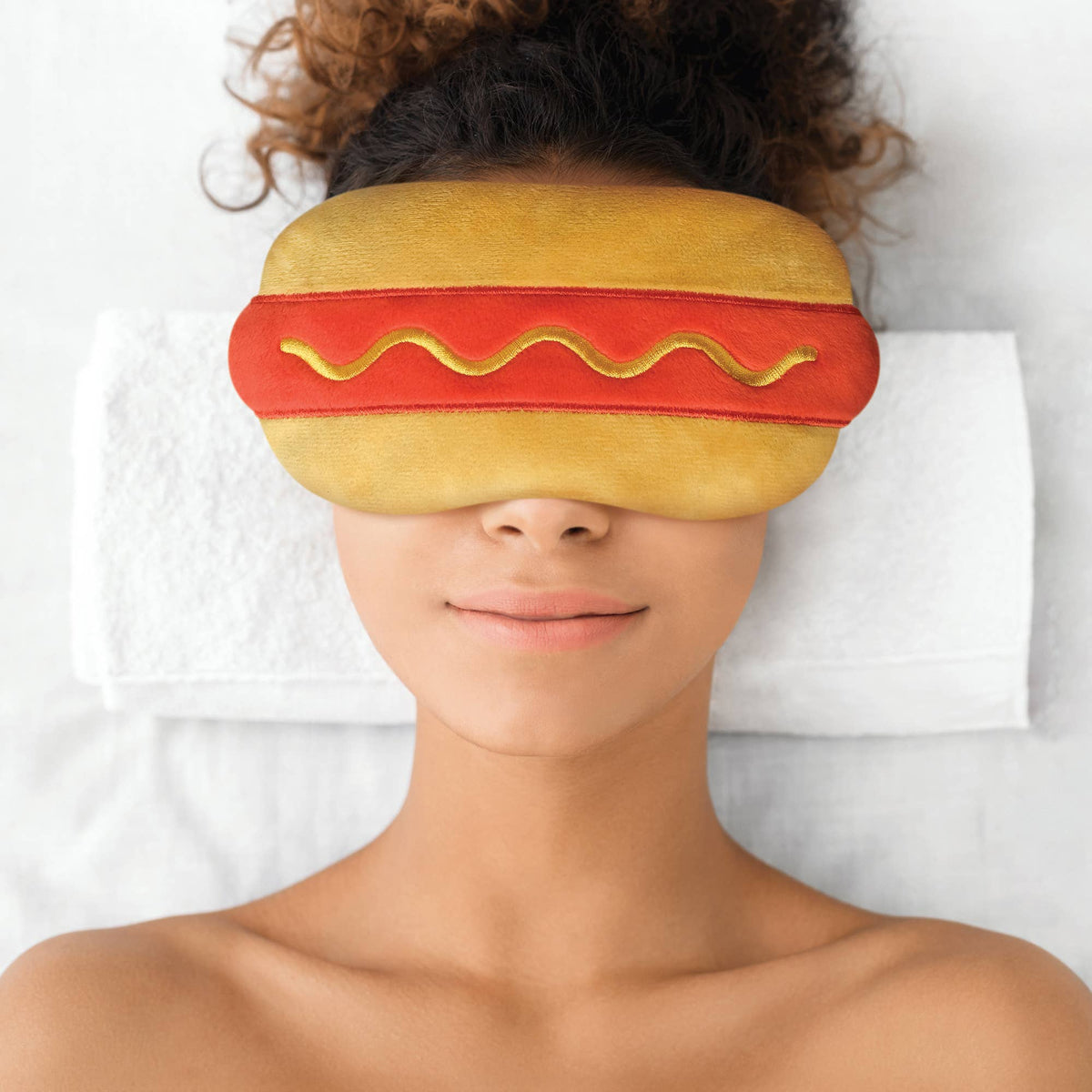 Person wearing a hot dog-shaped sleep mask on a white background