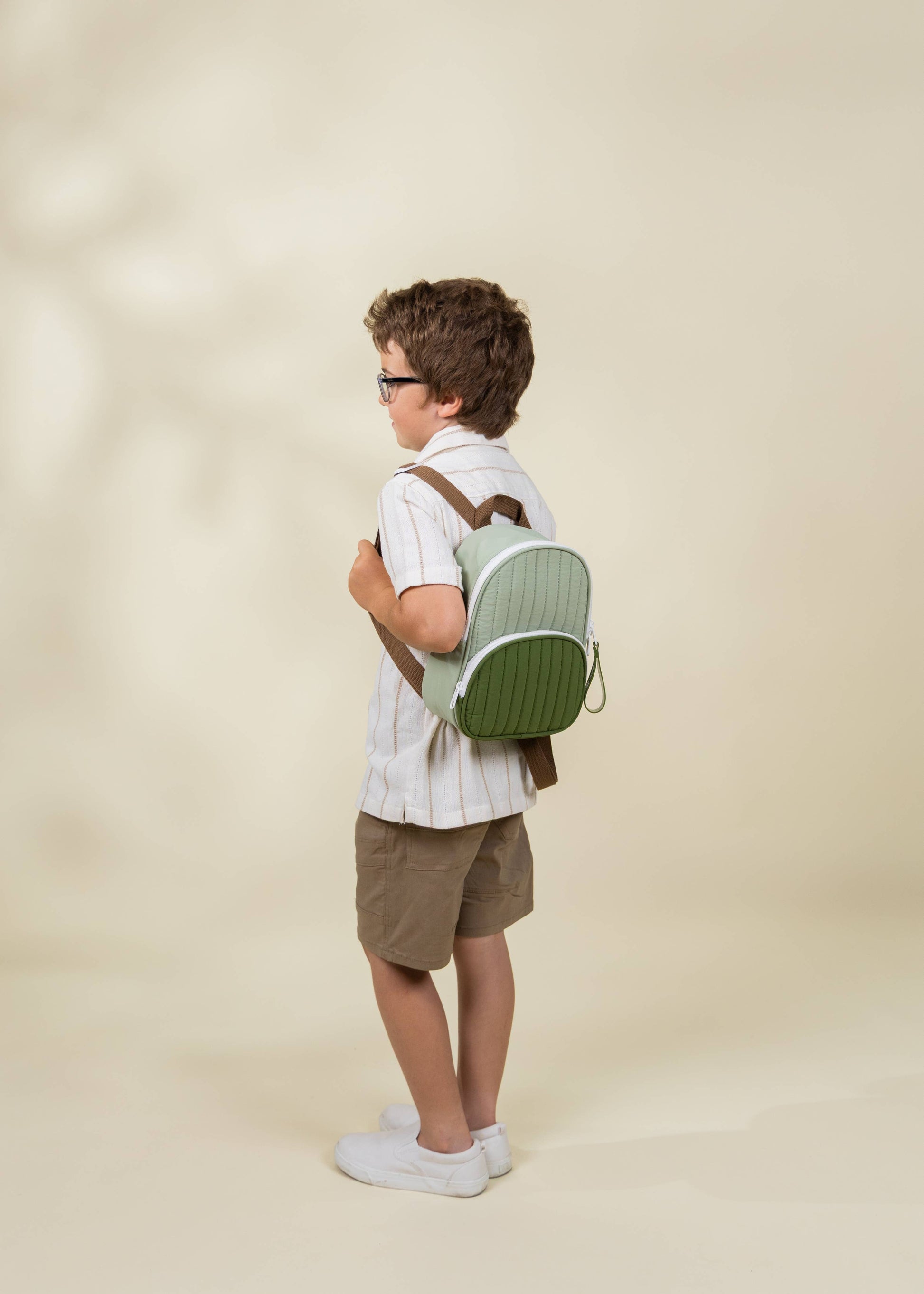 Child wearing a green backpack on a beige background