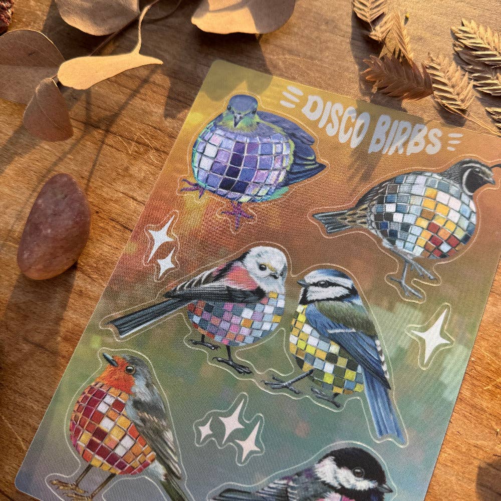 Holographic sticker sheet with bird designs on a wooden surface with leaves.