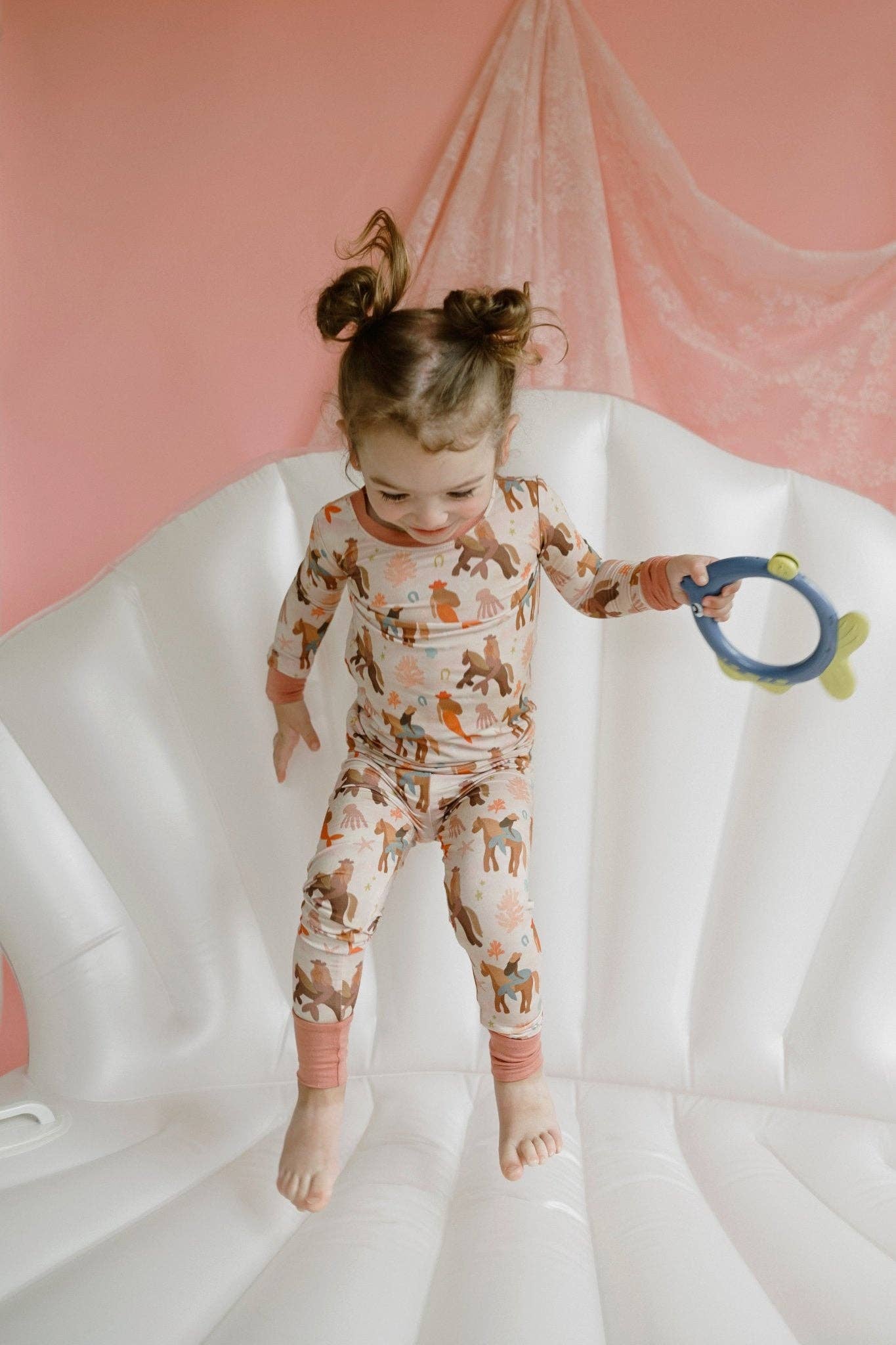 Child in a patterned onesie standing on a white surface with a pink background