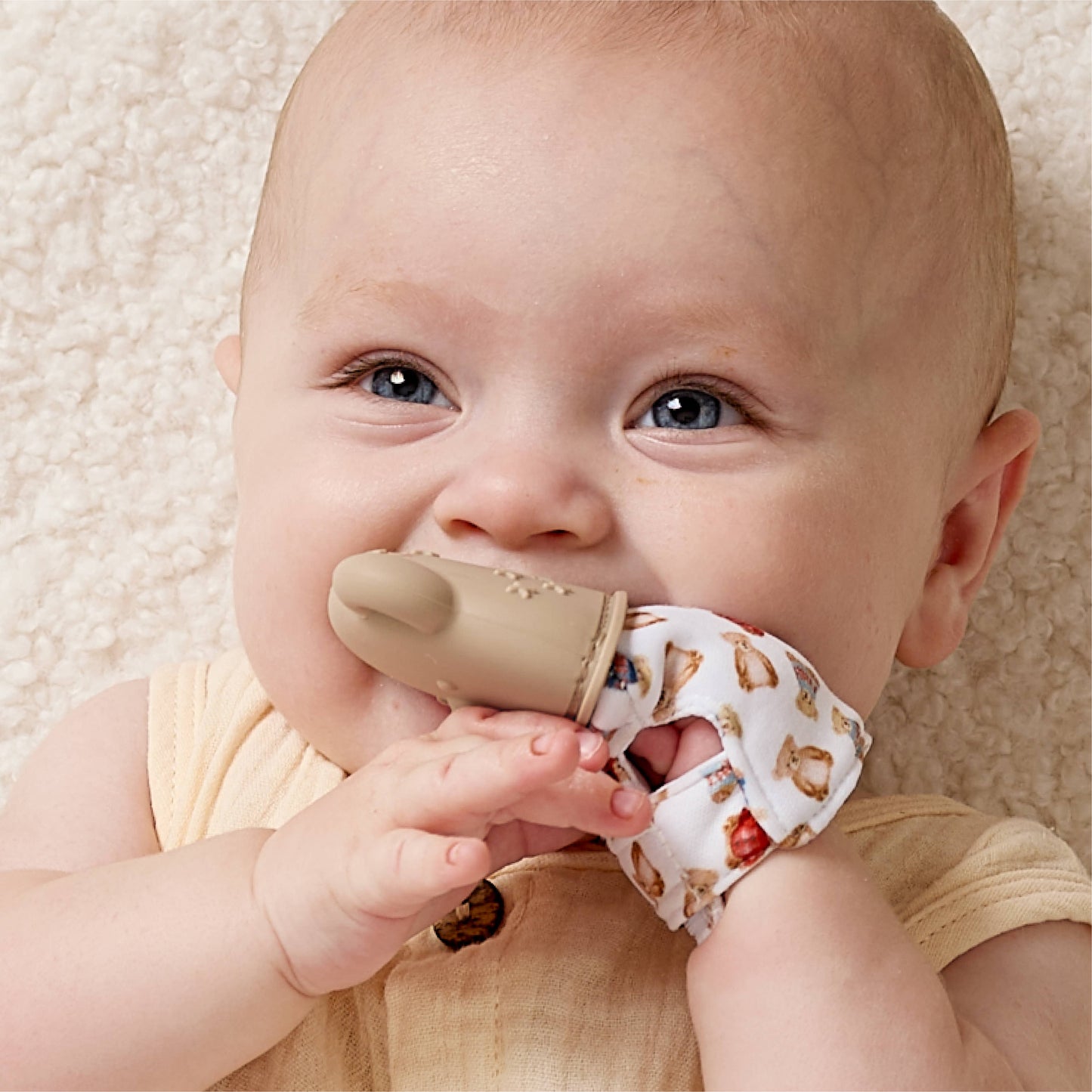 Baby holding a beige teething toy with a neutral background