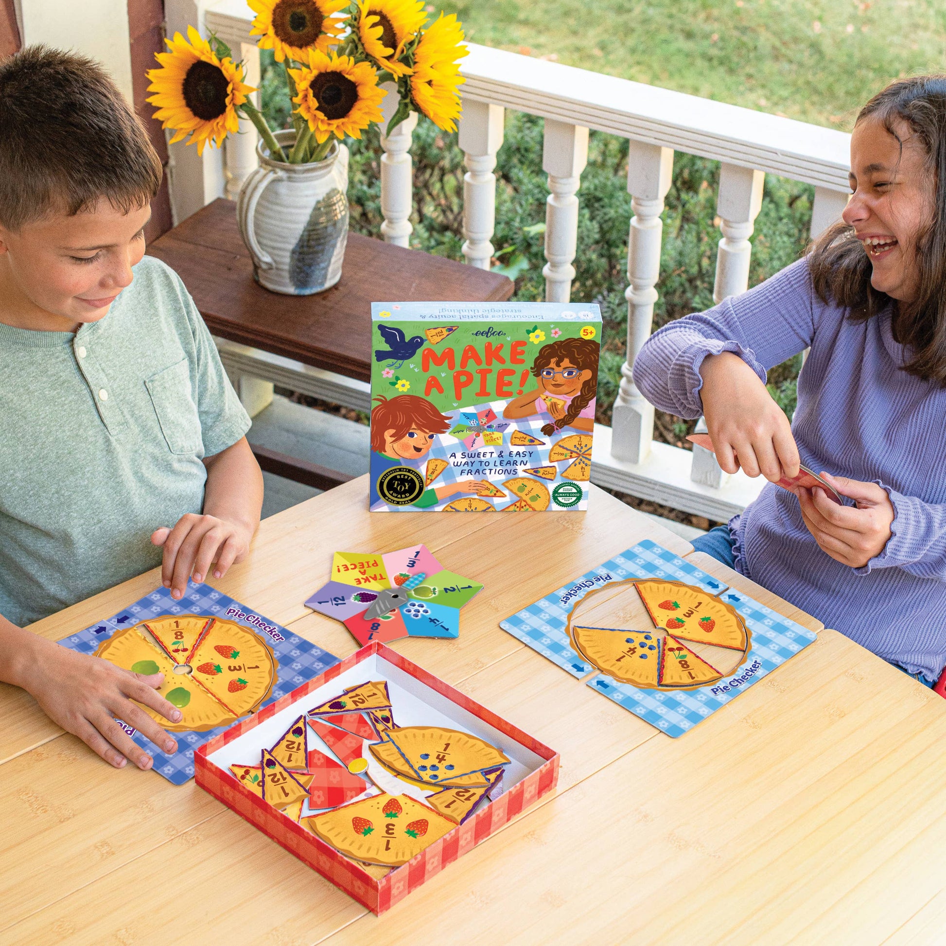 Two children playing with a pizza-themed puzzle on a wooden table outdoors.