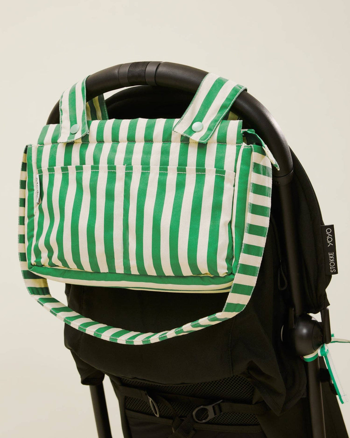 Green and white striped bag attached to a black stroller on a beige background