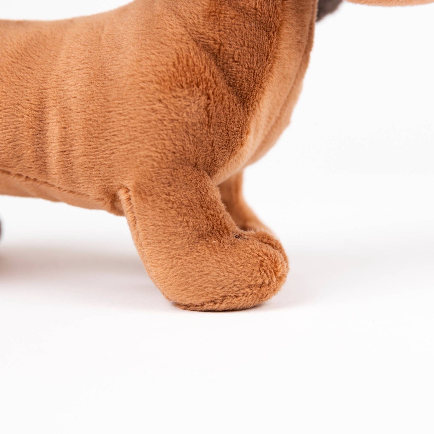Close-up of a brown plush dog toy, showing the soft textured fabric of its body and front paw on a clean white background.