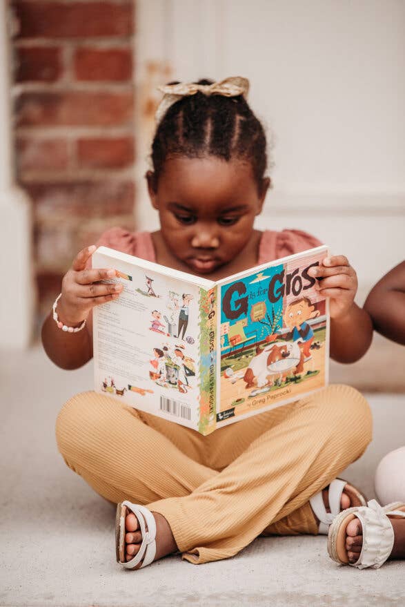 Child reading a book titled 'G is for...'