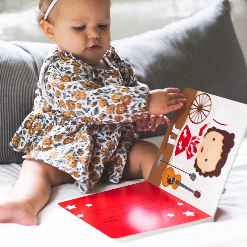 Baby in floral dress reading a book with illustrations on a couch