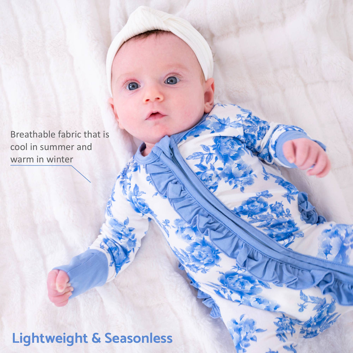 A baby lying on a white textured blanket wearing a white and blue floral long-sleeve footless sleeper with a ruffled front zipper and matching white bonnet. Text on the image highlights breathable fabric and lightweight seasonless design.