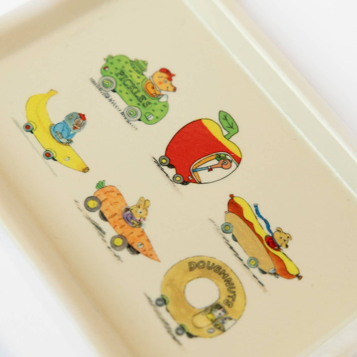 Colorful tray with cartoon characters driving food cars on a beige background