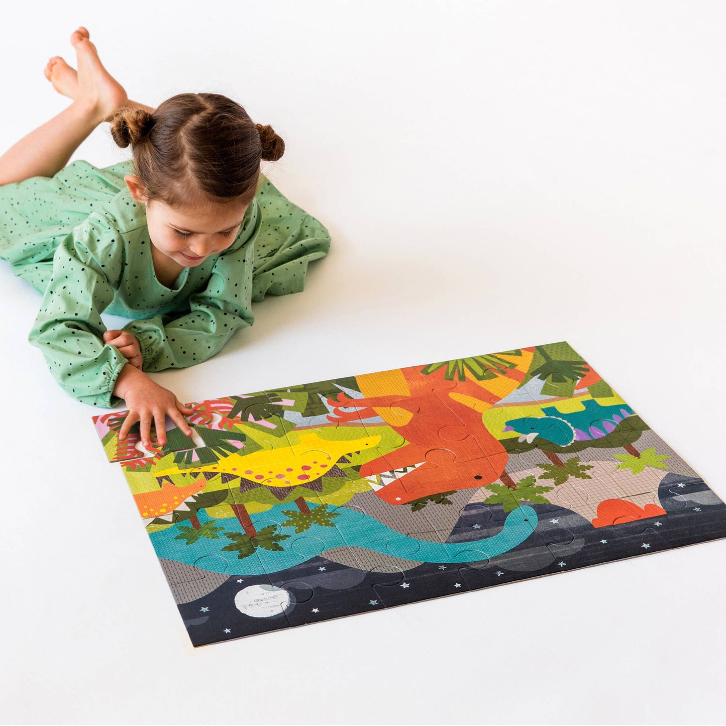 Child playing with a dinosaur-themed puzzle on a white floor