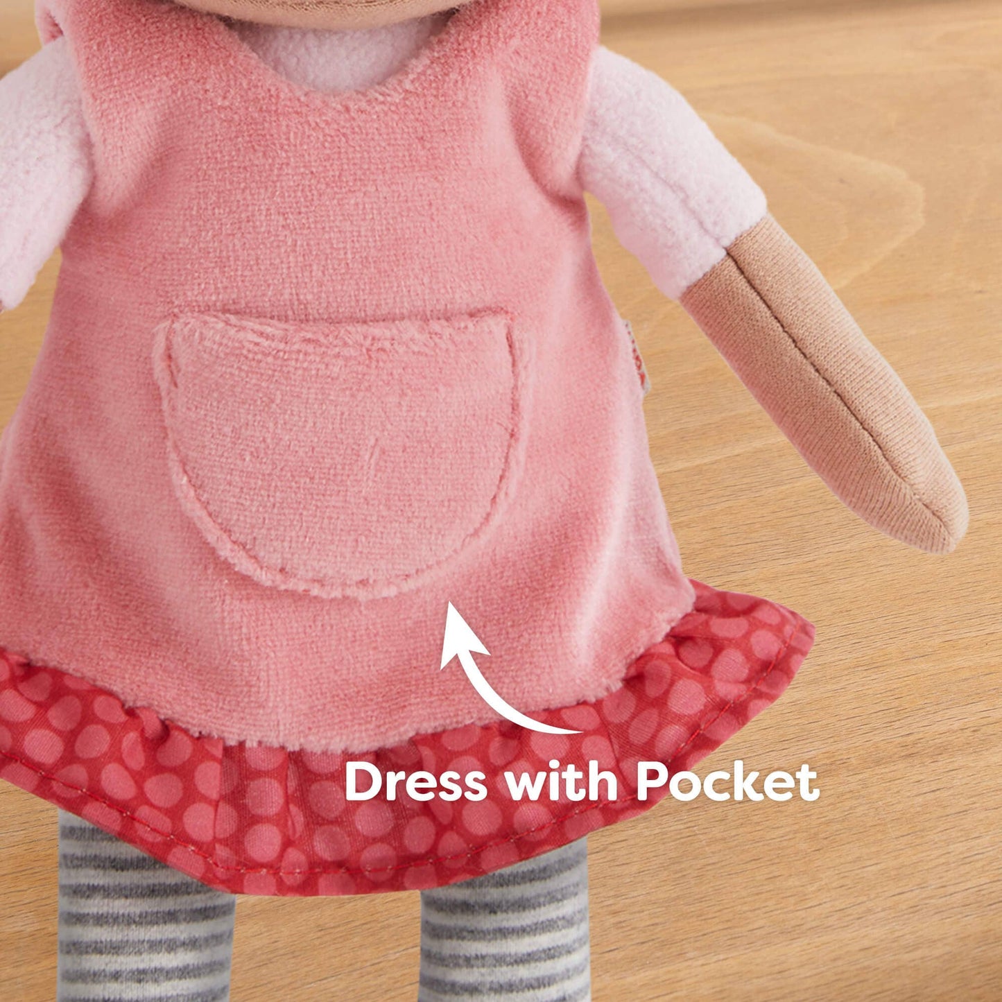 Toy figure wearing a pink dress with a pocket on a wooden surface