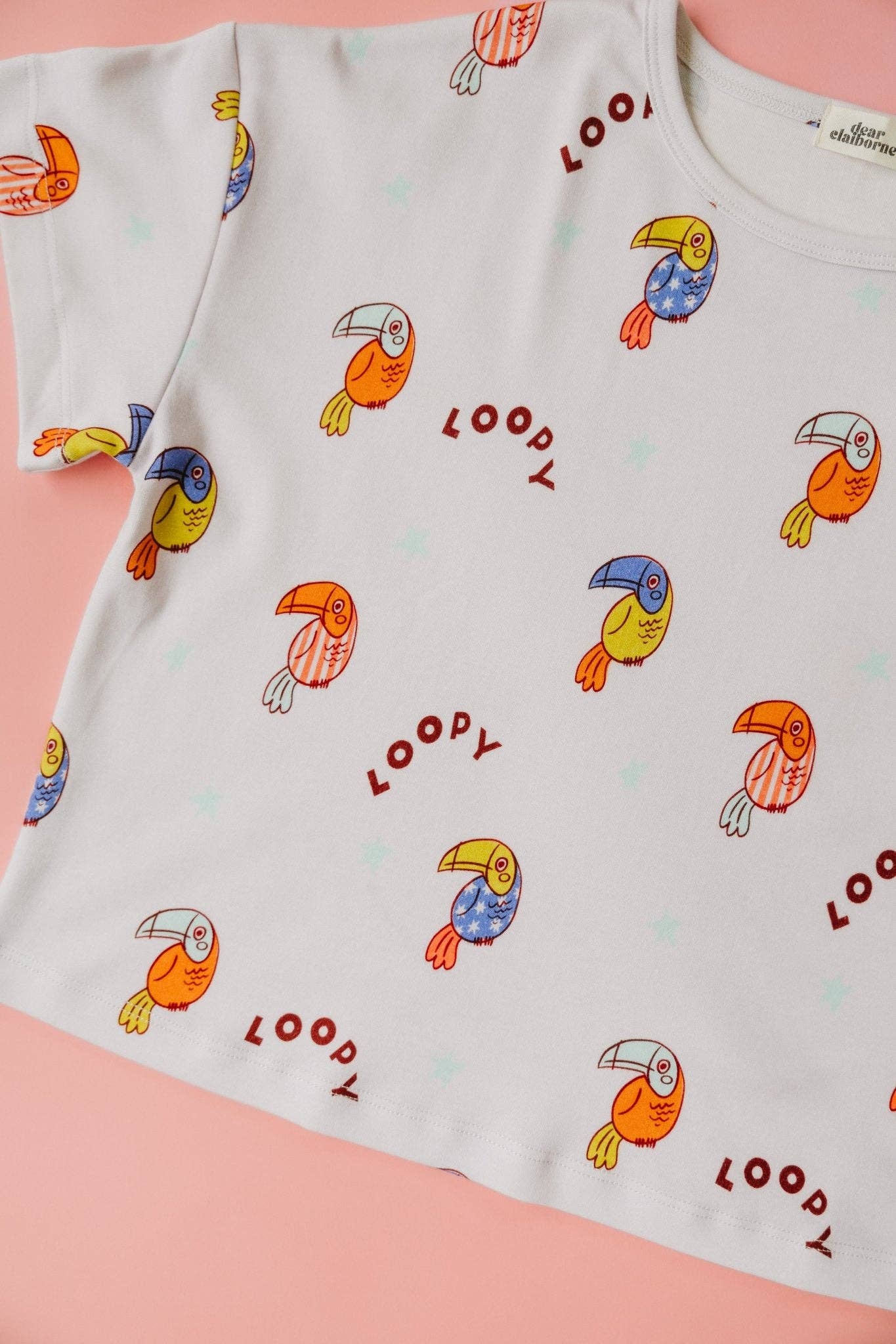 White t-shirt with colorful toucan patterns and 'Loopy' text on a pink background