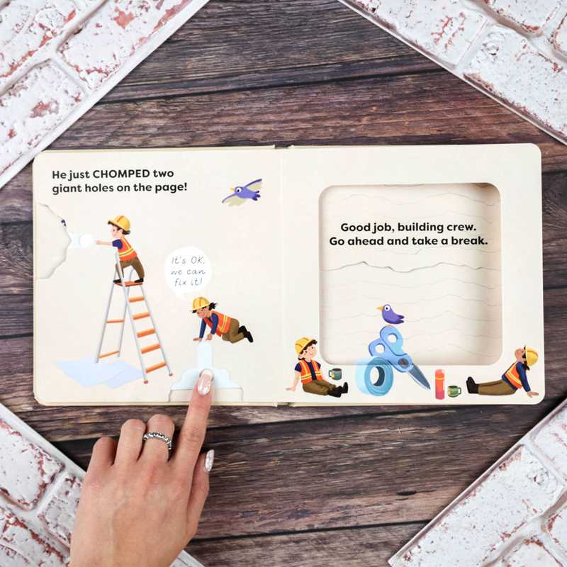 Children's book open to a page with illustrations of construction workers and scissors on a wooden surface.