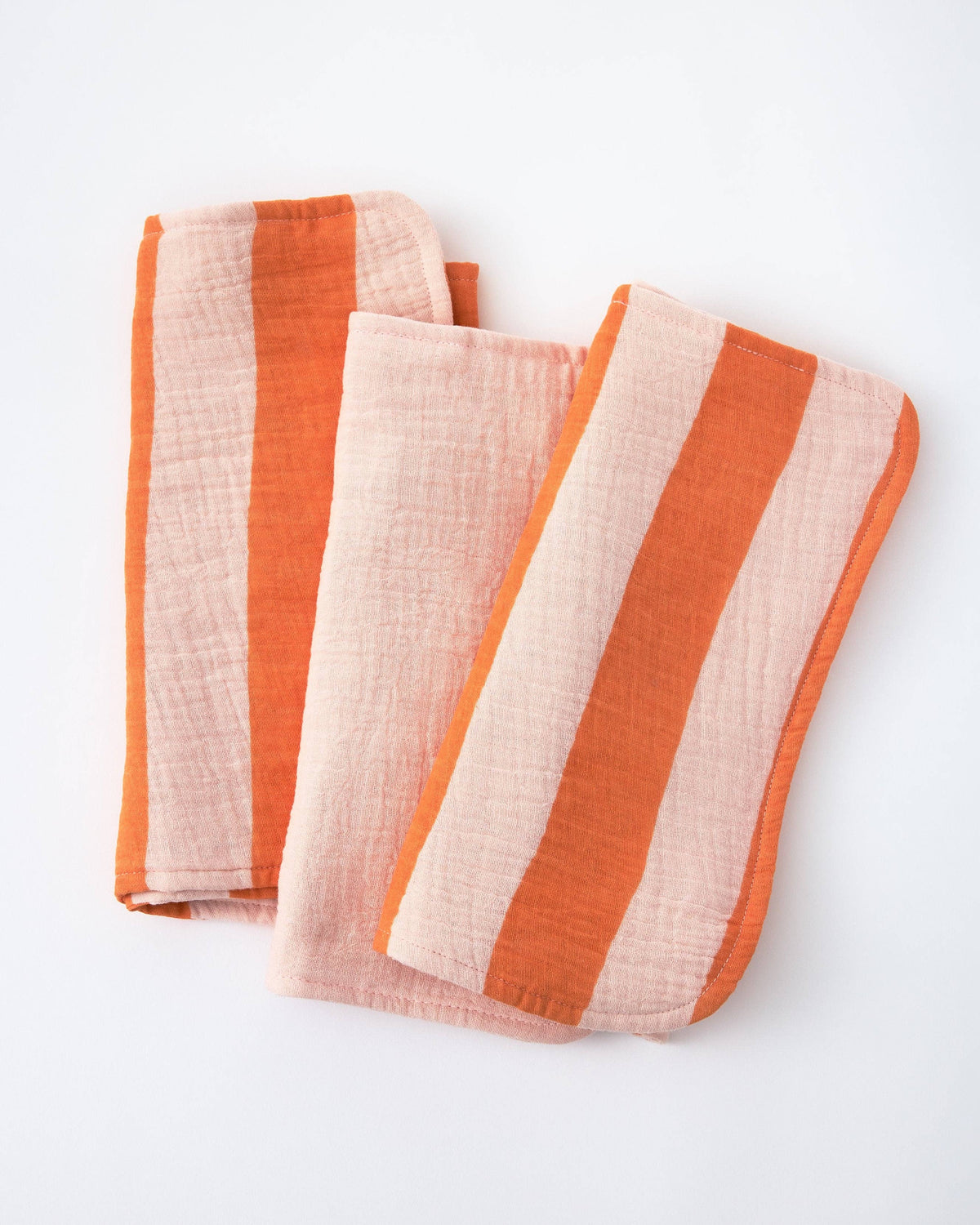 Two folded striped muslin cloths in orange and pale pink, displayed on a clean white background.