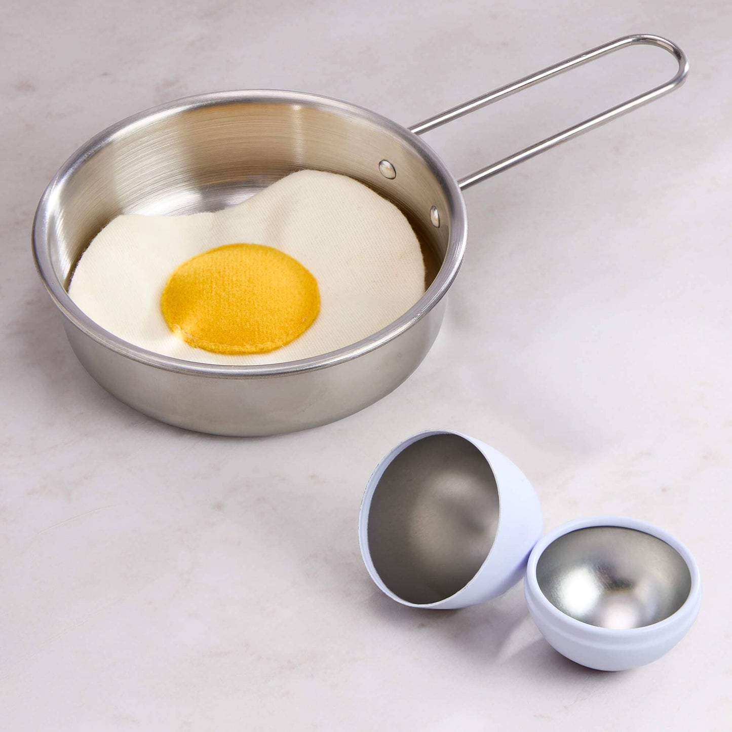 Metallic frying pan with an egg and two metallic egg-shaped molds on a light gray background