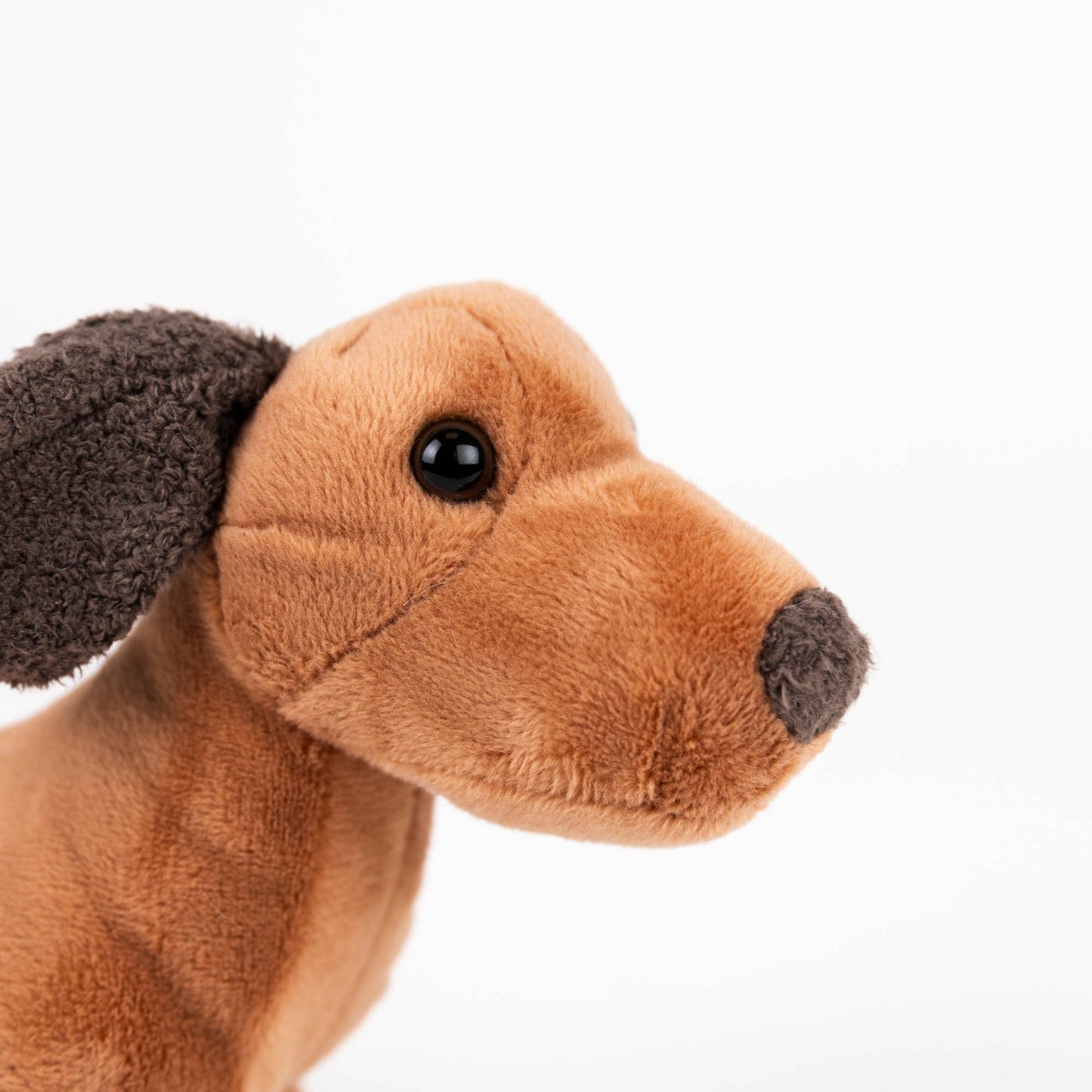 A close-up of a brown plush dog toy with dark brown ears and nose, shown in profile against a plain white background.