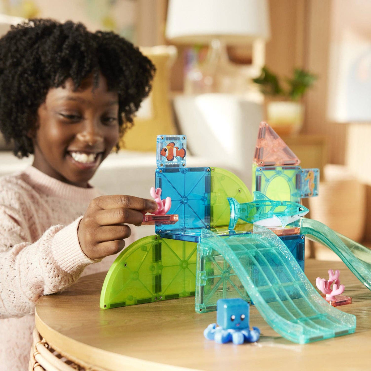 Child playing with a transparent toy set on a table, smiling.