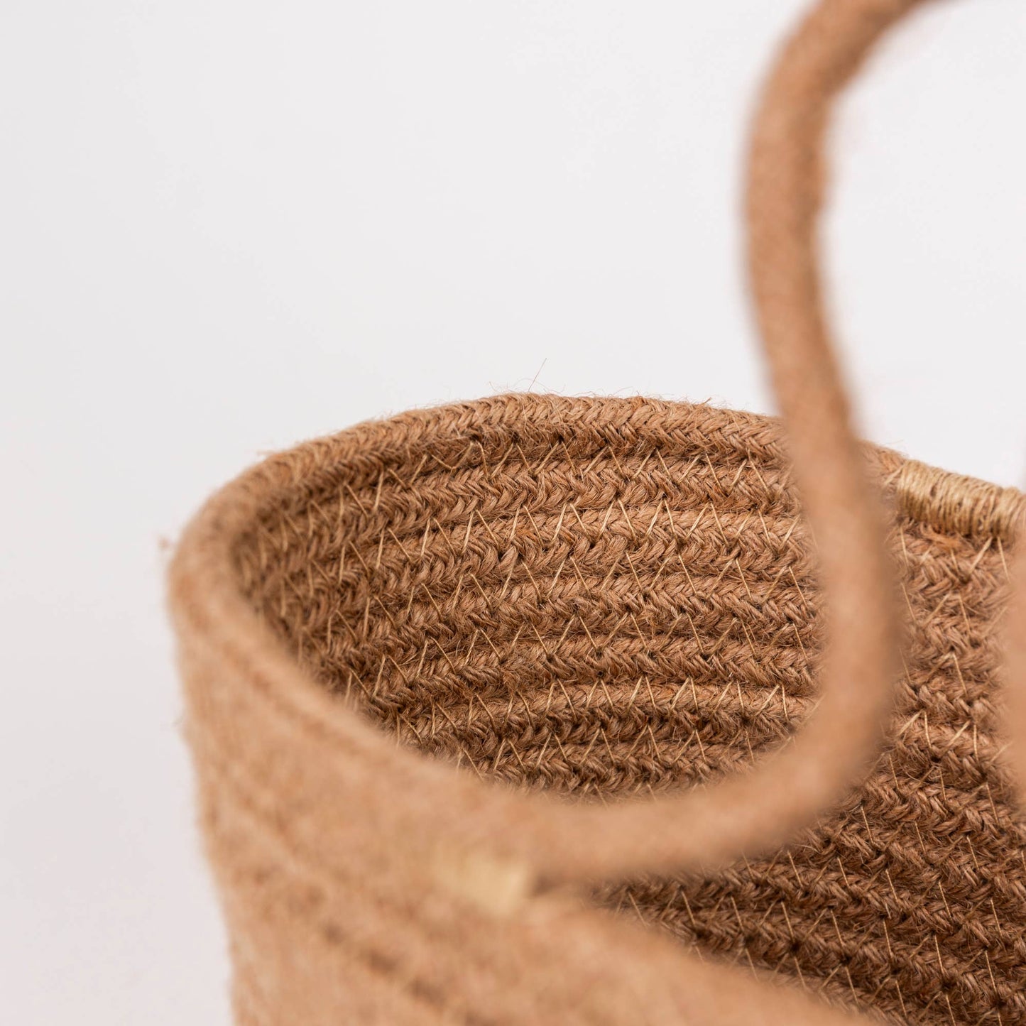 Close-up of a woven natural fiber bag with a thick rope handle, showing the textured straw material against a plain white background.