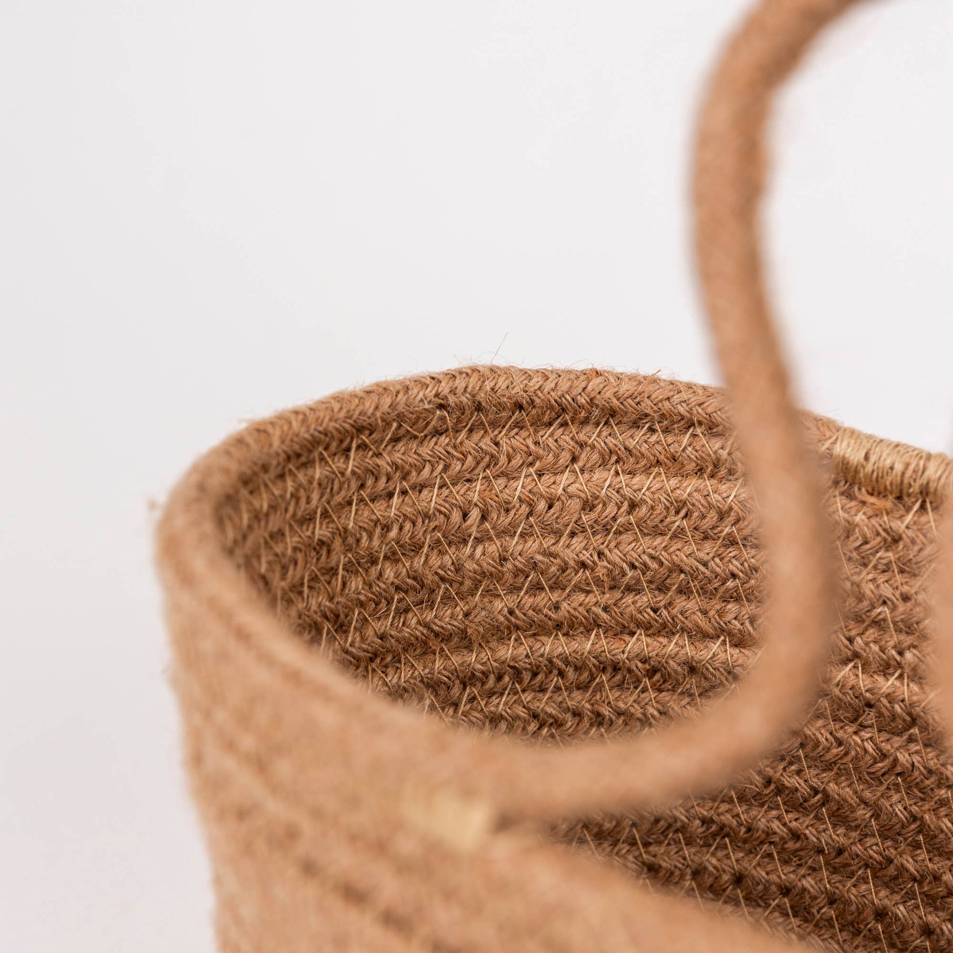 Close-up of a woven natural fiber bag with a thick rope handle, showing the textured straw material against a plain white background.