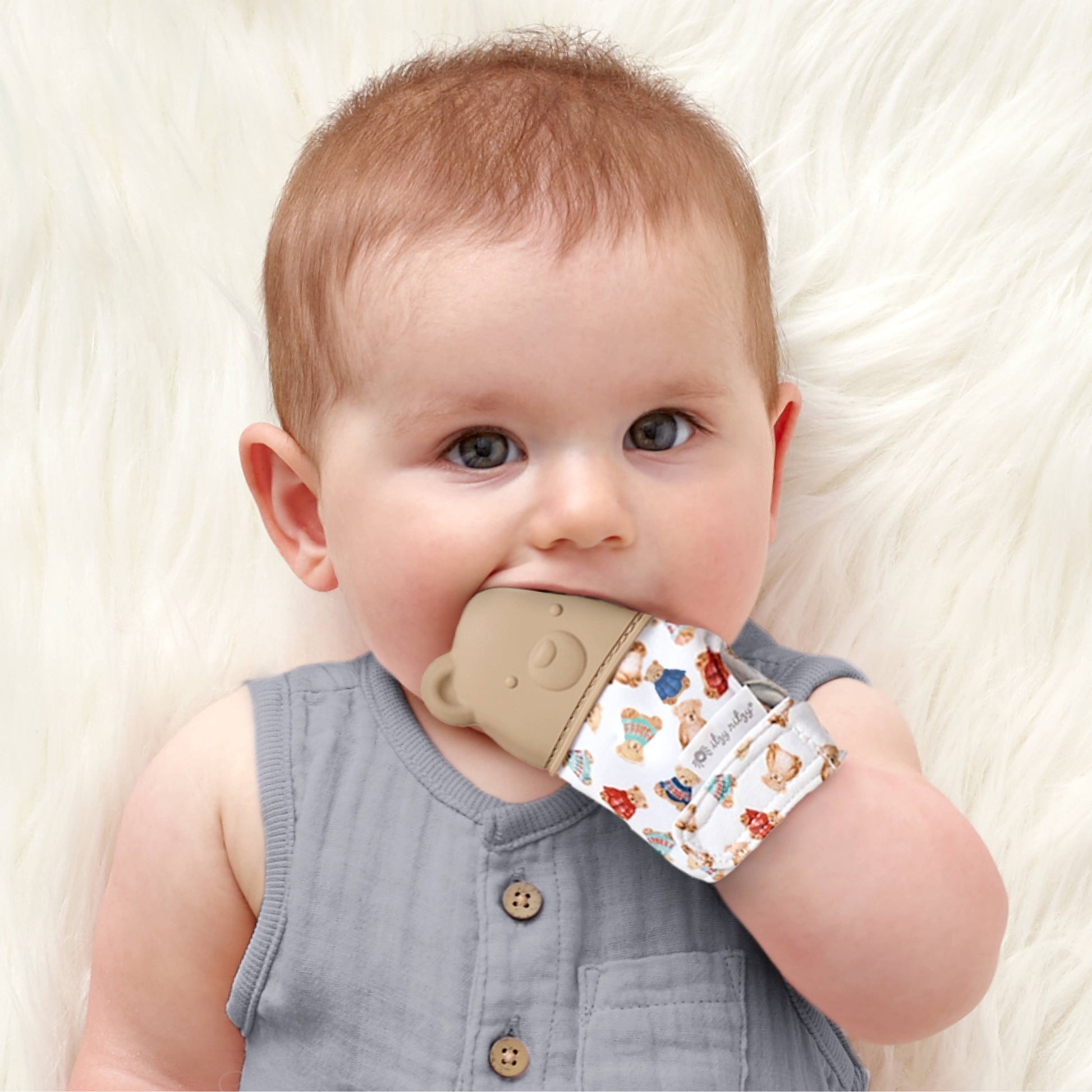 Baby holding a teething ring with a pattern of animals on a white blanket