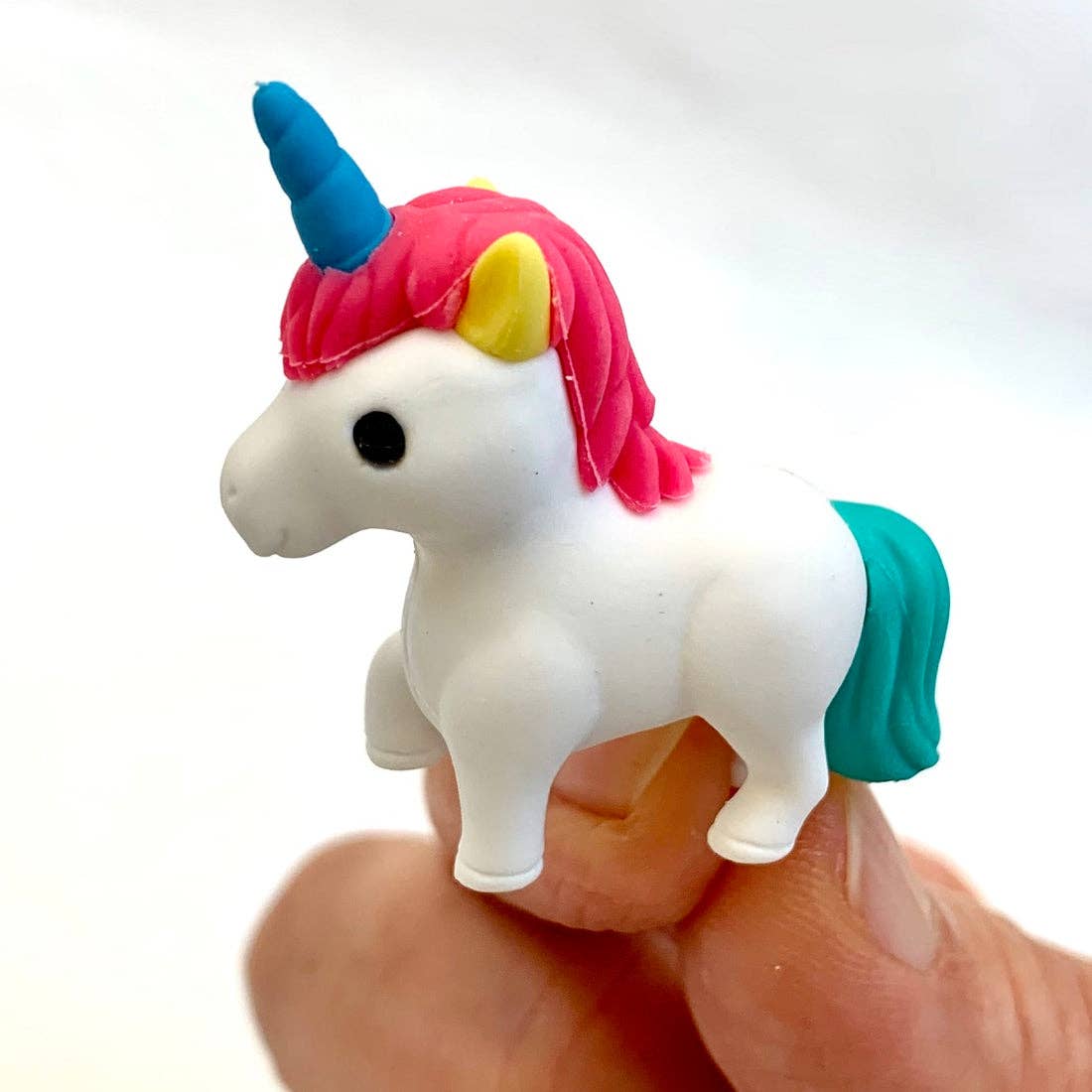 Small unicorn eraser figurine with colorful mane and tail held in a hand against a white background