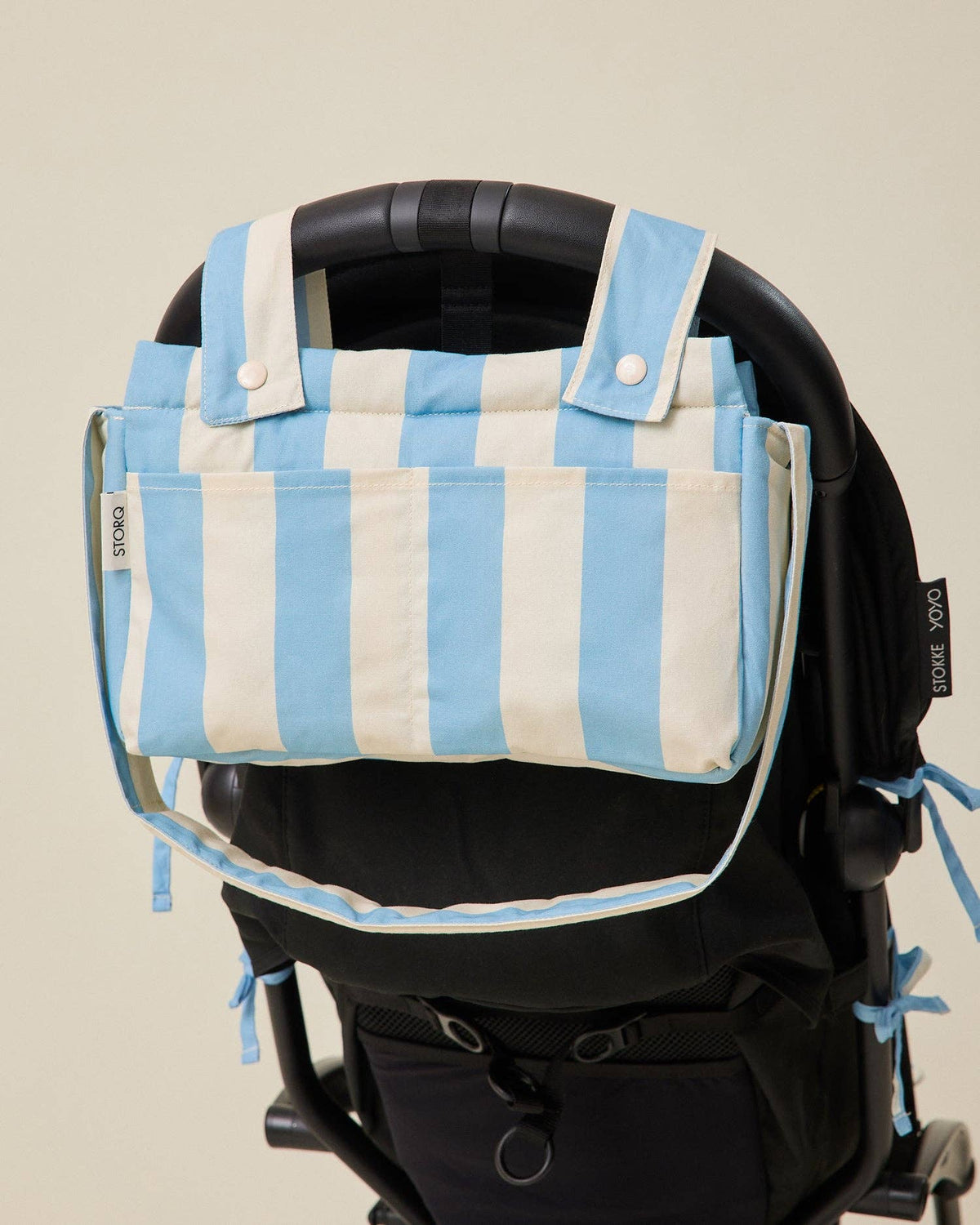Blue and white striped bag attached to a black stroller on a beige background