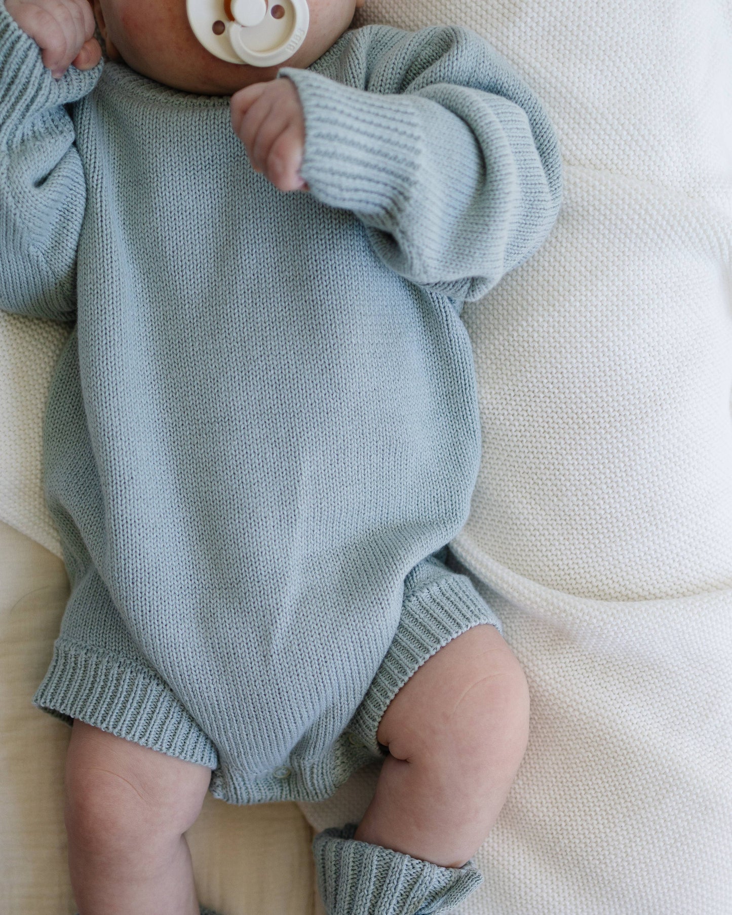 Baby wearing a light blue knitted outfit on a white blanket